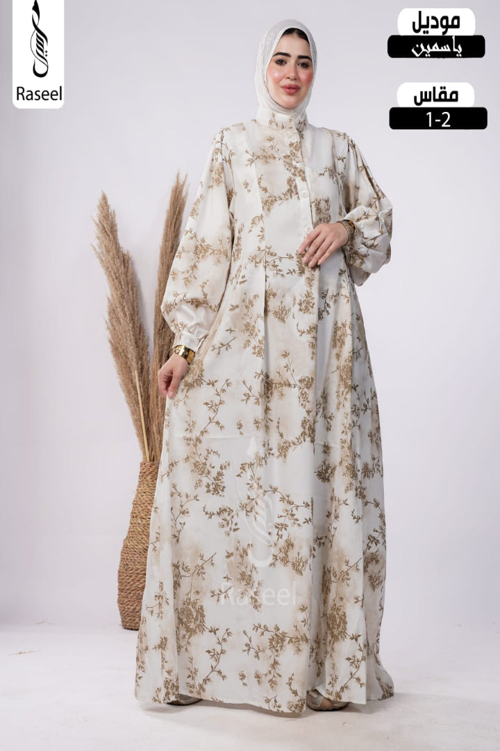 A woman modeling a long cream abaya with a brown floral pattern and a matching hijab, standing in a studio with decorative dried grass. The image includes text overlays for 'Raseel' and size information.