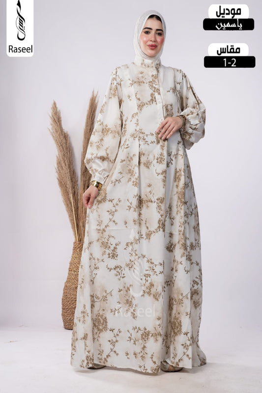 A woman modeling a long cream abaya with a brown floral pattern and a matching hijab, standing in a studio with decorative dried grass. The image includes text overlays for 'Raseel' and size information.